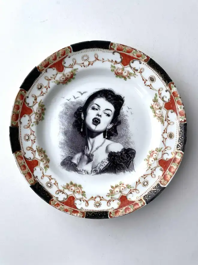 A vampire with bats behind her, the image is victorian in black and white and is printed directly onto an ornate vintage plate