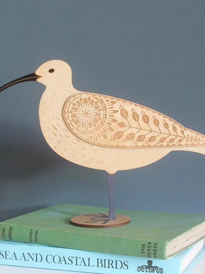 Standing Wooden Curlew, wooden bird decoration standing on a platform on a book. 