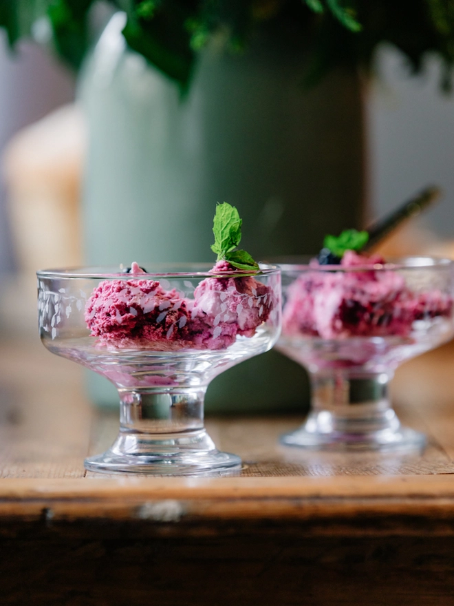 Two clear glass dessert bowls with an etched leaf pattern filled with ice cream and set on a rustic wooden table.