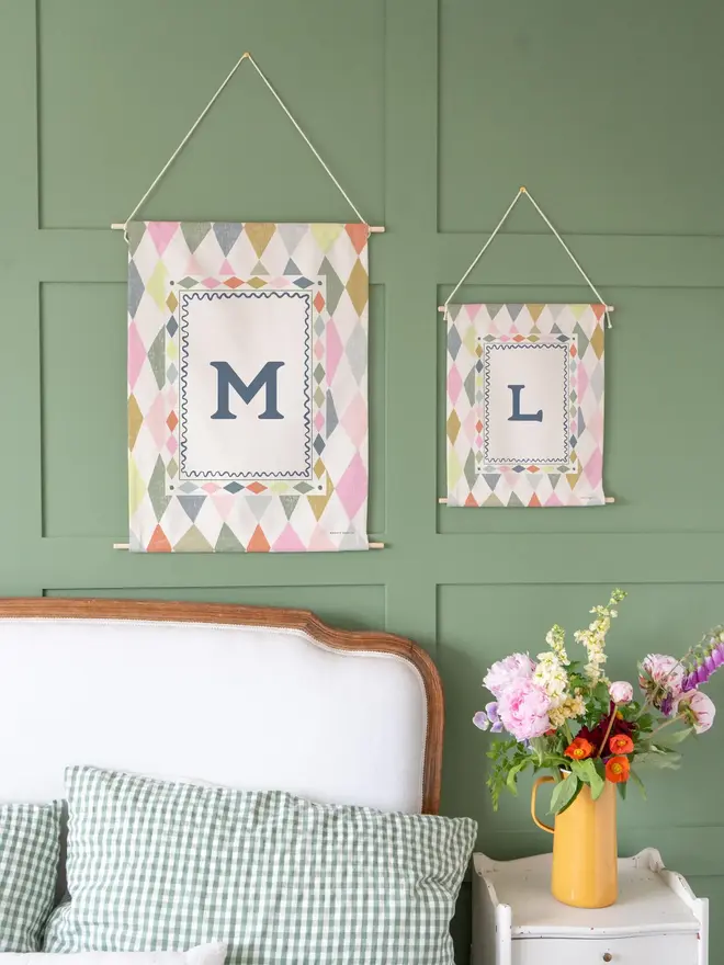 Harlequin Initial Fabric Banner, rainbow mini and midi next to each other against a green wall. 