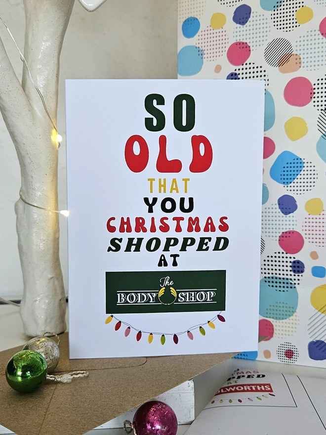 A photograph of the front of a humorous A6 greeting card illustrated using brightly coloured text and the retro shop logo. The text says so old  that you Christmas shopped at The Body Shop with string lights