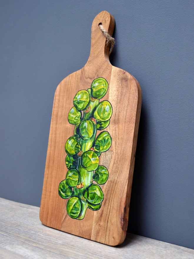 A wooden serving board with a handpainted design of Brussels sprouts