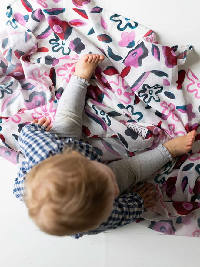 Abstract Flowers Muslin. A muslin with a purple abstract flower design, spread out with a baby next to it.