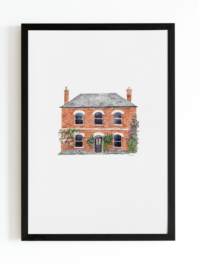Black frame with white page inside and a beautiful red bricked period detached house sits in the centre, painted in intricate watercolour details. There is beautiful wiseria to the right and a yelow climbing rose over the door. 