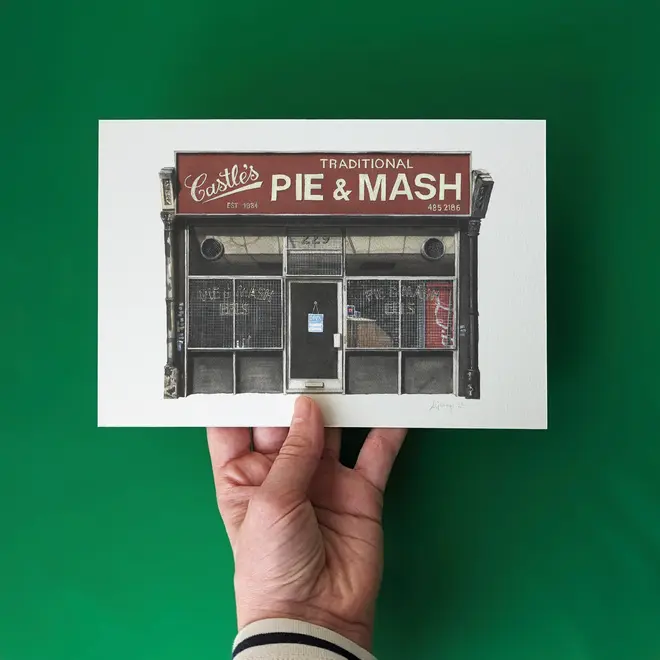 Camden Castle's Pie & Mash Shop Giclée Print (Unframed), a print of a shop held against a green backdrop by a woman. 