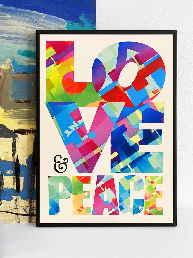 Framed multicoloured typographic print of “Peace & Love”  The print rests against a blue and yellow abstract painting.