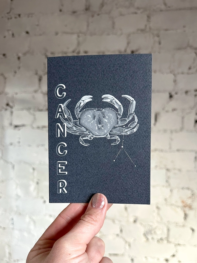 a greetings card featuring a greyscale illustration of a zodiac style crab with the text “CANCER”