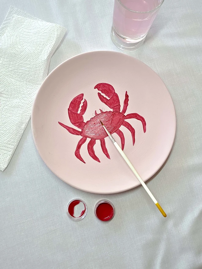 half painted crab design on plate with brush, paint water and cloth
