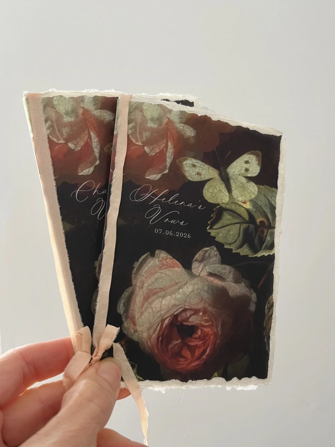 Beautiful handmade paper vow books with a romantic butterfly and rose design printed on a vellum cover. Antique effect faux silk ribbon tied in a bow holds all the pages together.