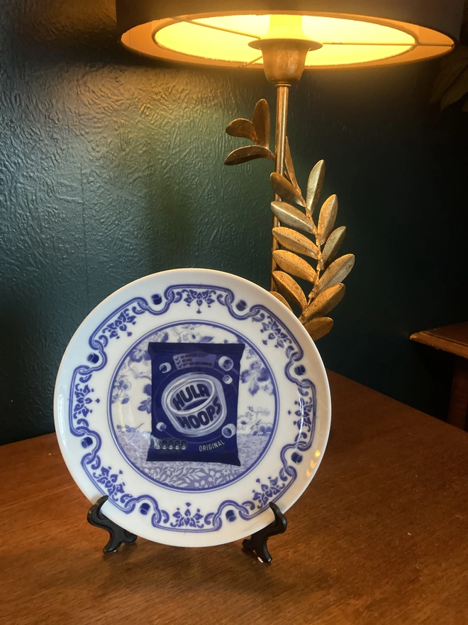 Blue and white Delft style decorative plate featuring a packet of Hula Hoops crisps in the centre.