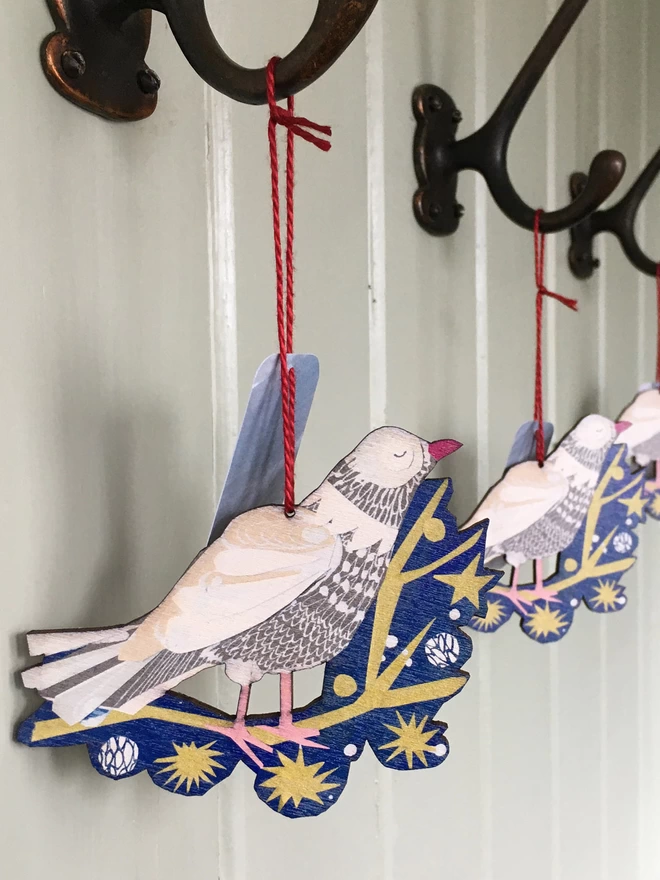 Three illustrated peace dove decorations hang from red thread on old iron hooks