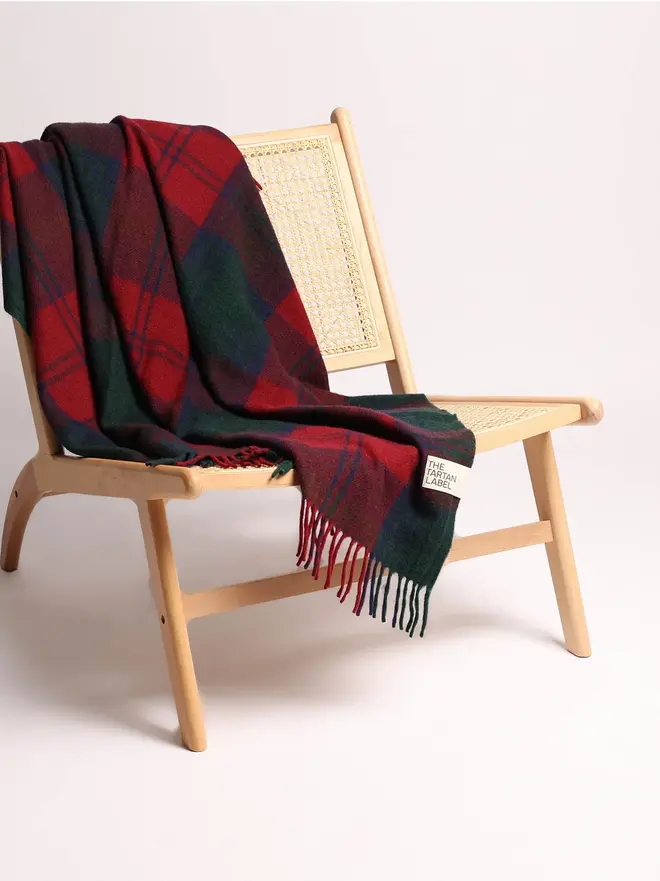 Lindsay Tartan Blanket, a red blanket draped over a wooden chair on a plain surface against a white backdrop. 