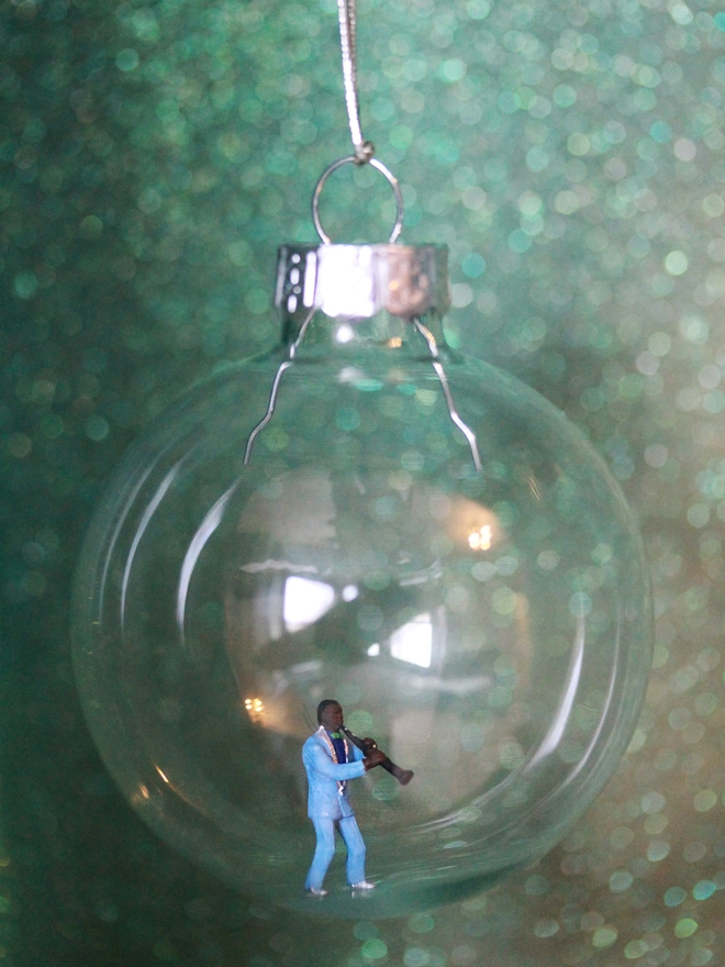 Miniature figure of a man playing a clarinet in a glass Christmas bauble - close up 