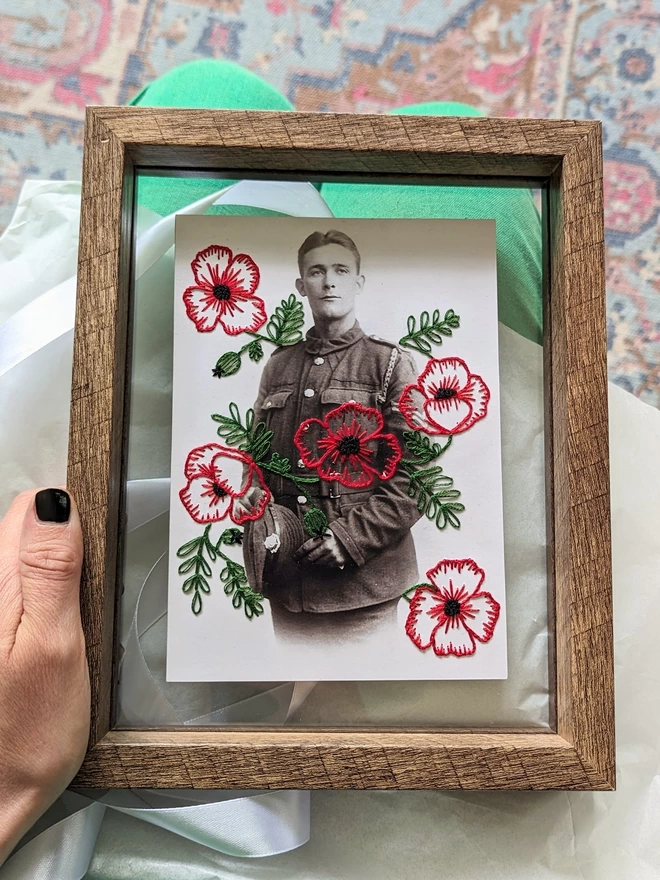 Embroidered red poppies on b&w photo of man in uniform held in double glass frame