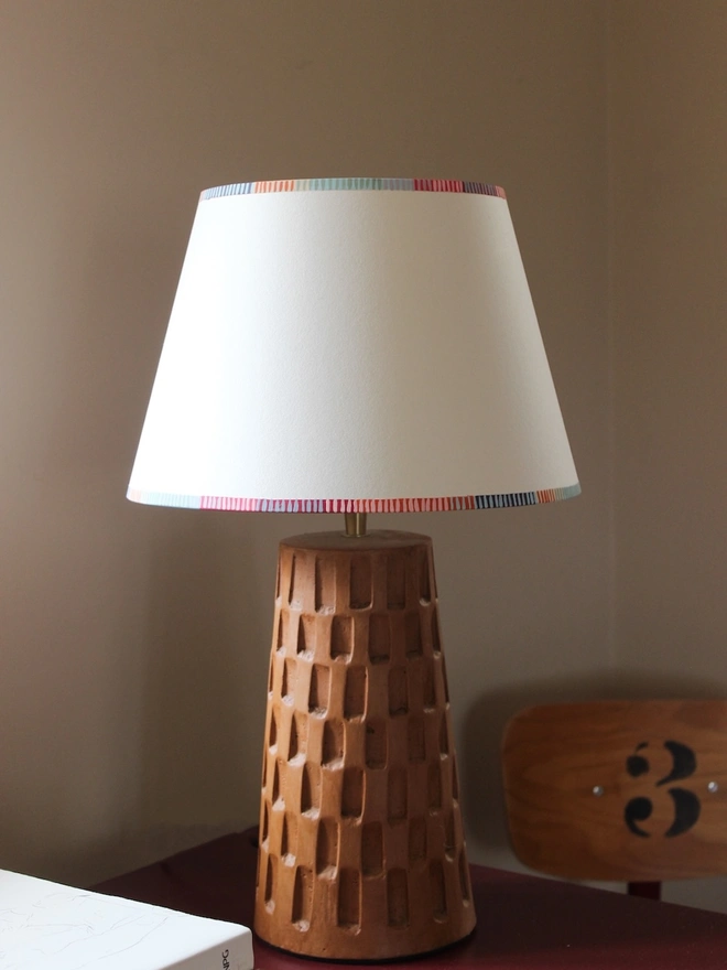A colourful lampshade with bold striped trim, styled on a geometric wooden lamp base. This empire lampshade showcases striped lampshades UK craftsmanship.