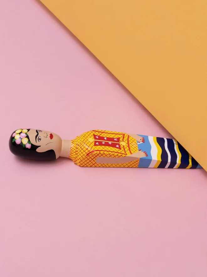 Wooden Door Stopper (Freeda Floral Crown Outfit), a colourful wooden door stop sitting under a door.