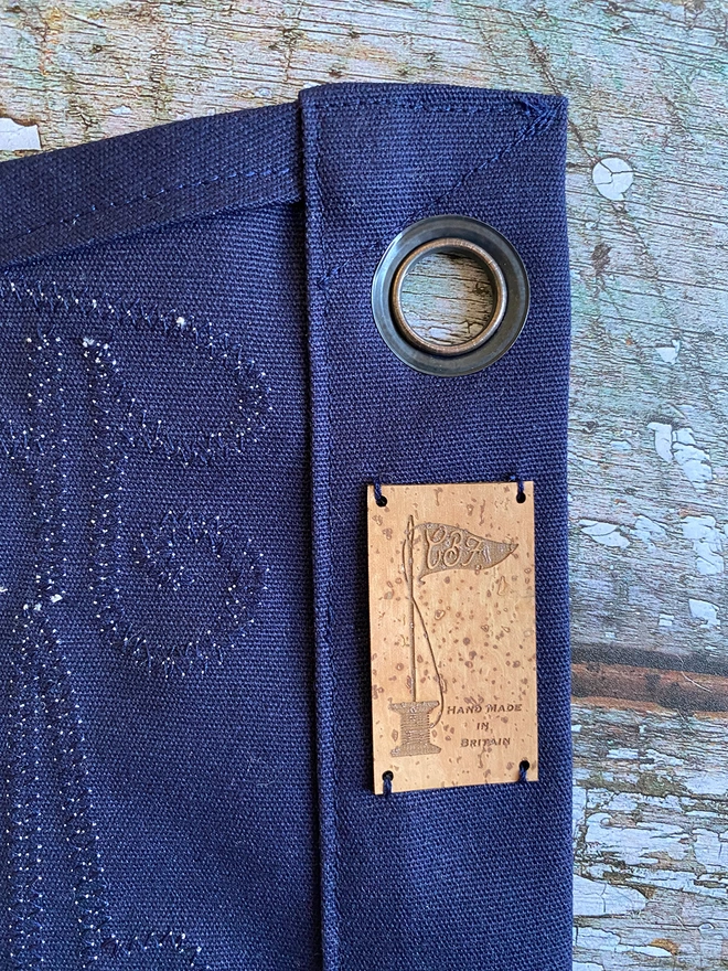 A closed up of the back of a navy pennant flag showing the stitch work, an eyelet and cork label.