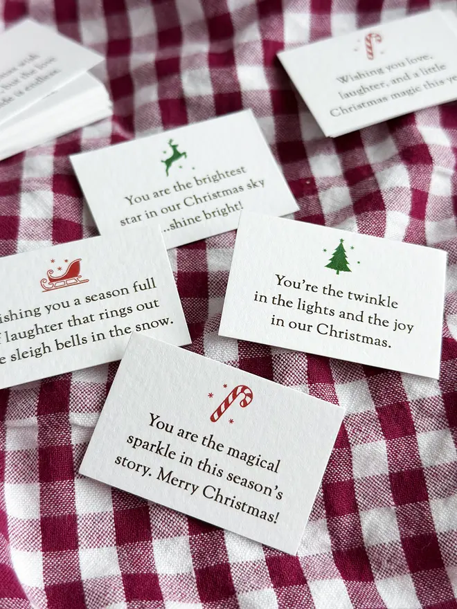 Several tiny Christmas wish cards, each with a festive illustration and a Christmas wish, lay on a gingham tablecloth.