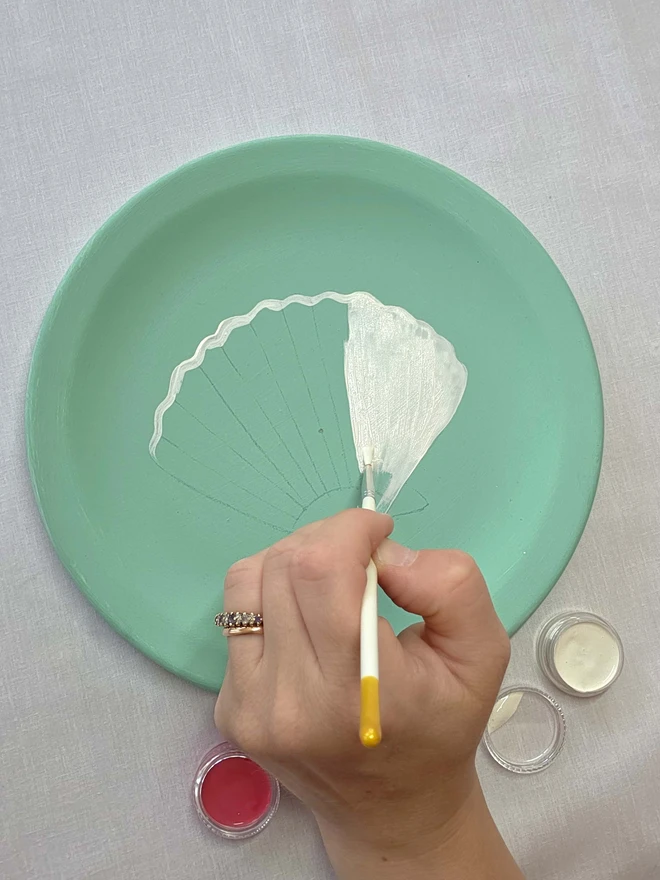 hand painting a shell design on mint plate