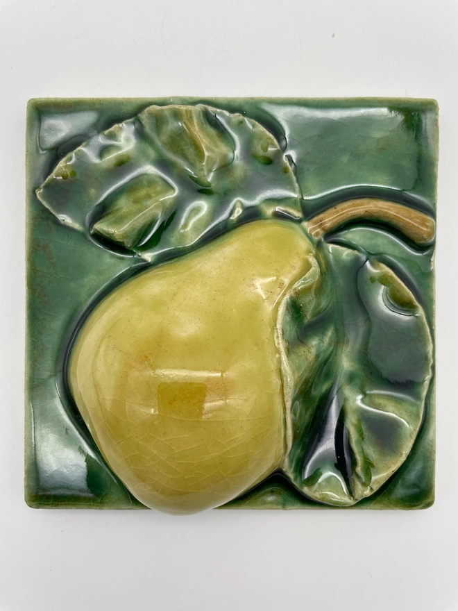 Handmade ceramic tile taken from a plaster cast of a real pear, side view with stalk and two leaves. Very realistic, three-dimensional, with lush coloured glazes.