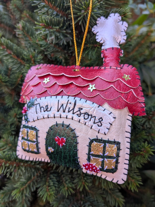 Hand stitched personalised Christmas house decoration made from vegan-friendly faux leather, featuring a red roof, gold stars and a family name banner.