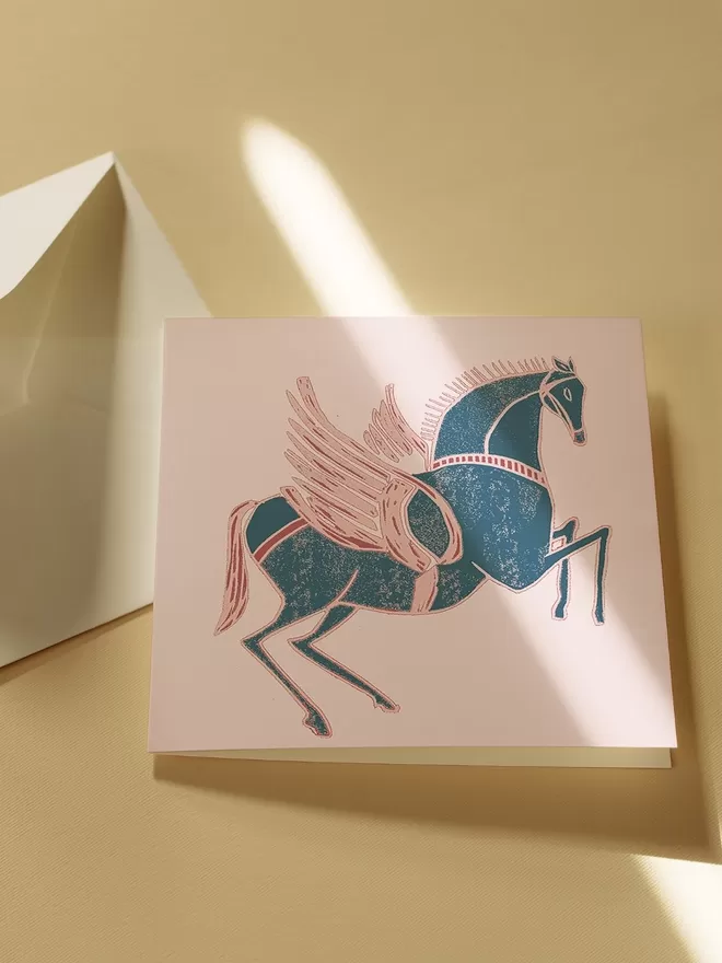 Annika Reed Studio woodblock print of a blue and pink winged horse seen on a card.