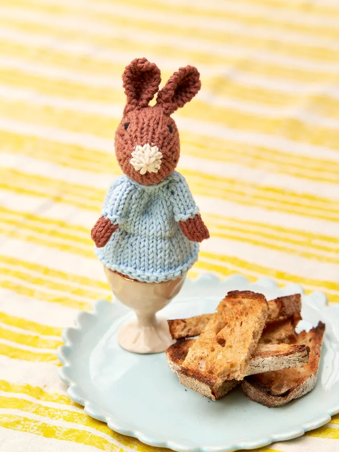 Egg Cosy Rabbits Easter Table Decoration, a colourful Easter cosies sitting on a wooden surface. 