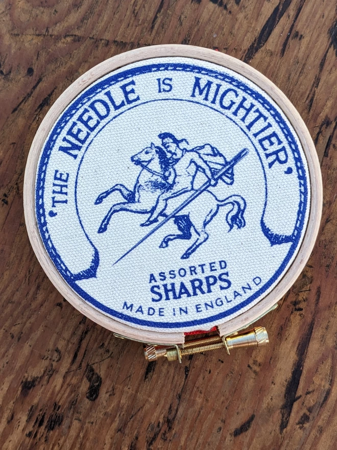 Royal blue coloured 'the needle is mightier' embroidery hoop needle book depicting a soldier on horse back with a needle as a sword