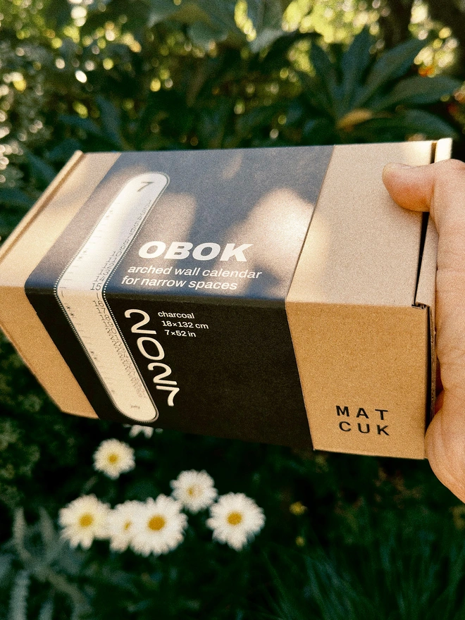 Obok 2027 Arched Wall Calendar packaging in hand against greenery.