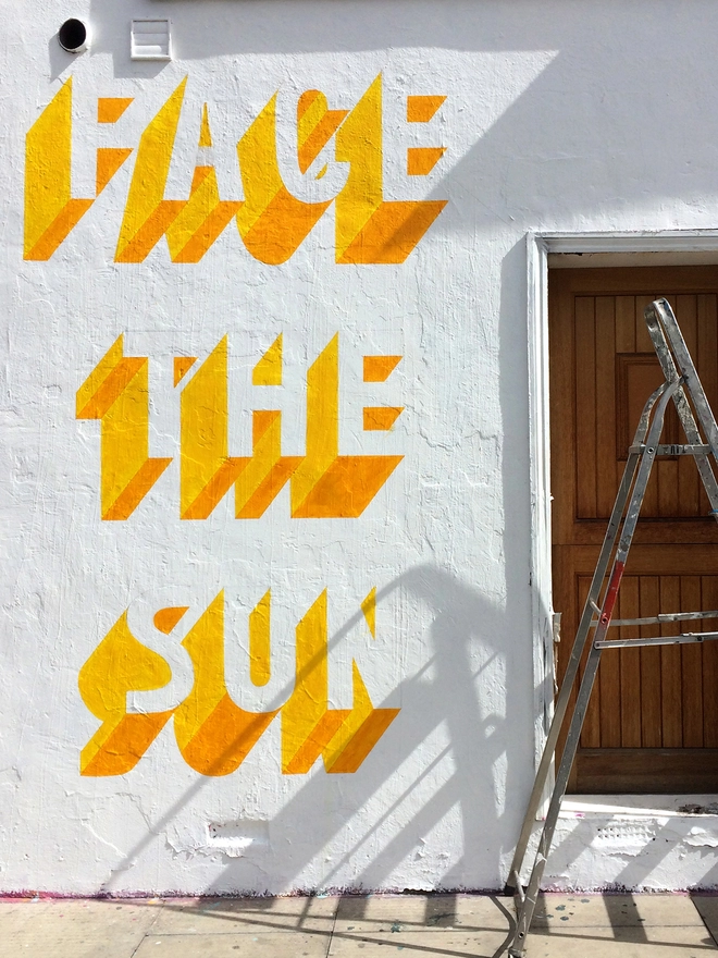Detail shot of a Survival Techniques street art painting in progress with 3d typography of the words Face The Sun and a ladder
