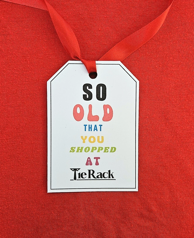 A gift tag that says so old you shopped at Tie Rack written in brightly coloured fonts with a red ribbon