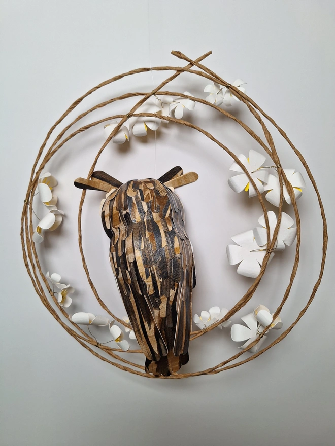 back view of a long eared owl sculpture, perched on a wreath of paper blossom