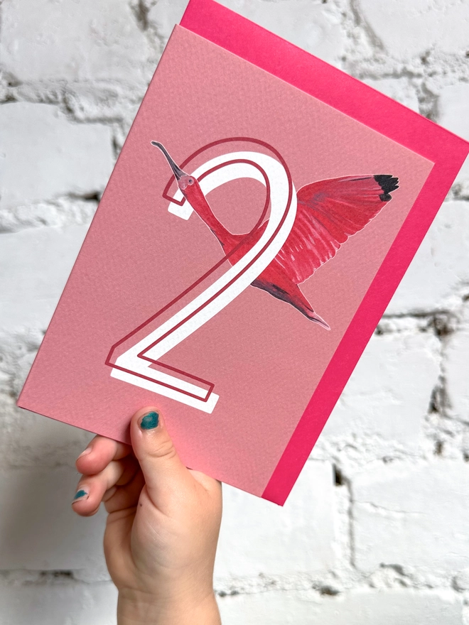 a pink card with a big white number 2 and an illustration of a scarlet ibis with a neon pink envelope