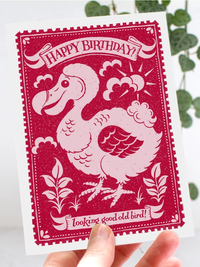 hand holding pink dodo birthday card with small leaves in background