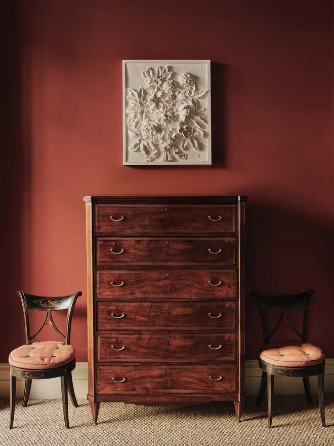 Plaster bas-relief wall plaque with flower design above a wooden cabinet with red wall behind