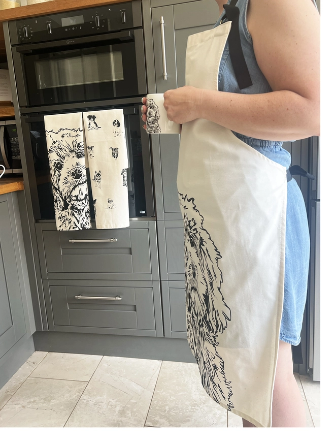 Matching Cockapoo apron being worn next to a folded hanging cockapoo tea towel