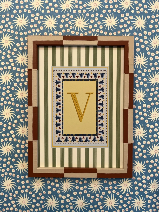 A collection of colourful hand painted bobbin and striped frames with letter prints inside surrounded by a striped border. Colourful wall art display by annabel wond interiors. 