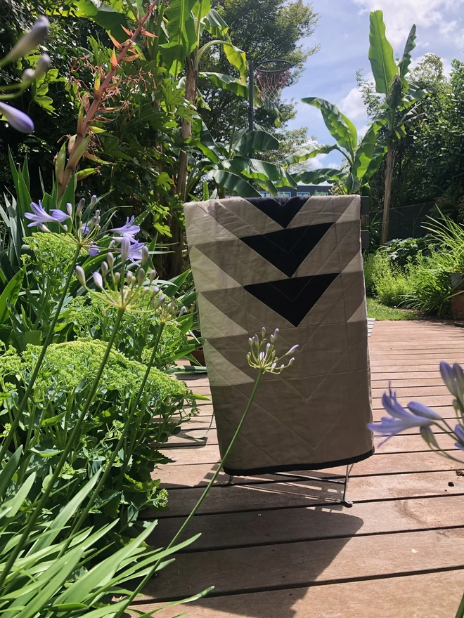 Flow Taupe Linen Throw Quilt. A natural quilt with bold triangle pattern. Folded on garden chair for summer evening.