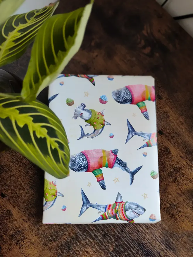 illustrated sharks in jumpers wrapping paper sheet. a sheet of cream wrapping paper featuring illustrated sharks in wooly jumpers.