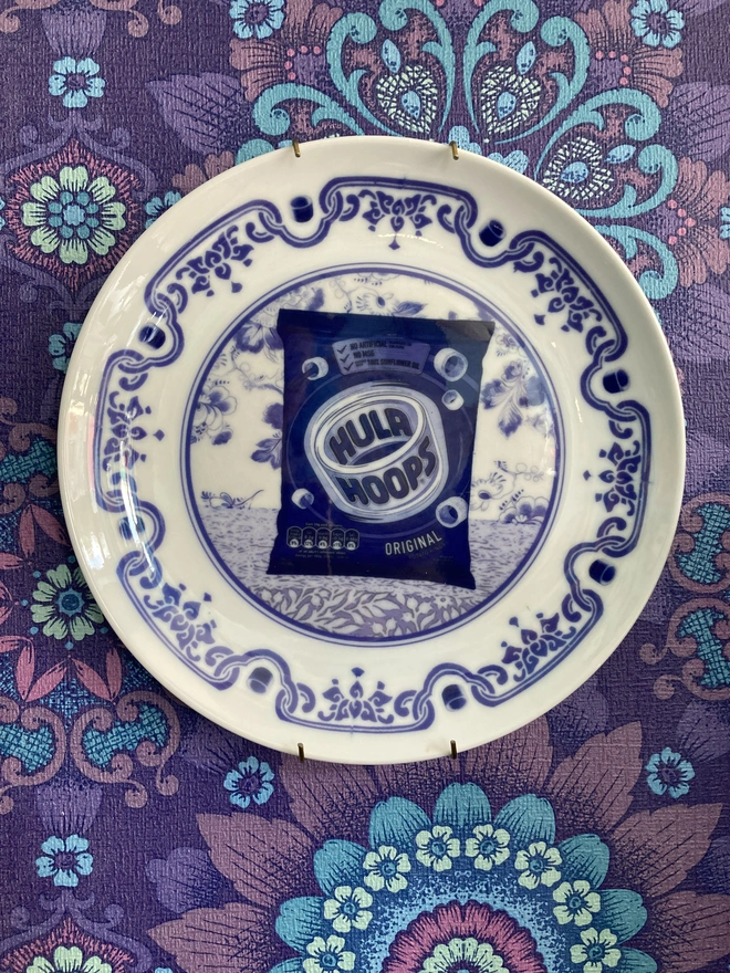 Blue and white Delft style decorative plate featuring a packet of Hula Hoops crisps in the centre.