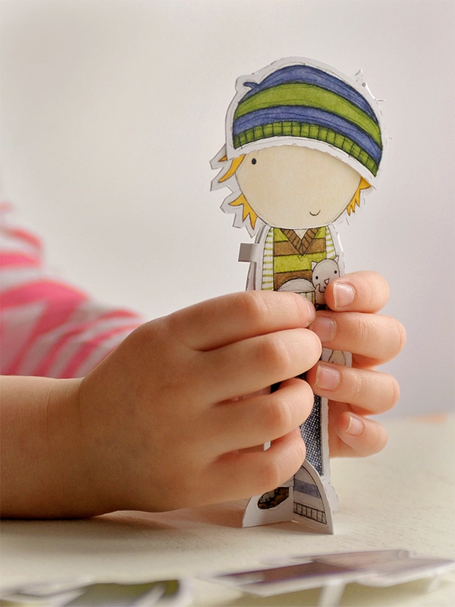 A young child is playing with a paper doll, dressing it in paper outfits.