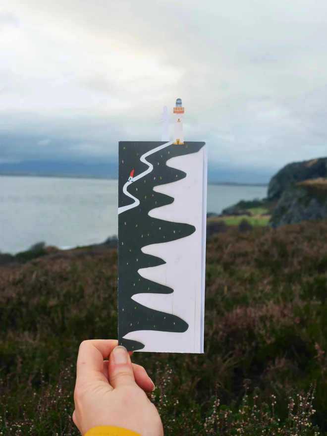 A cut out card of a cliff with a cliff and the sea in the background