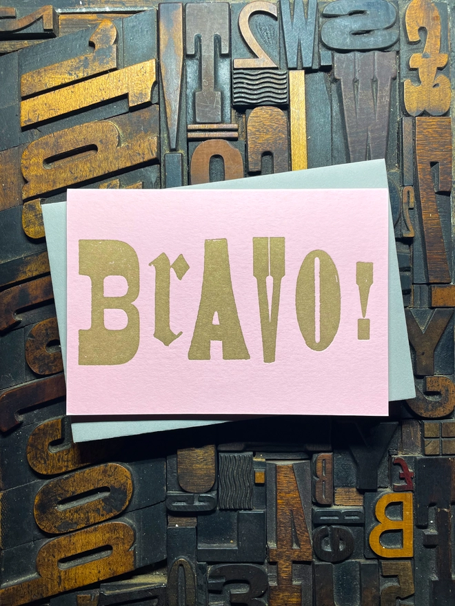 A congratulatory letterpress candy pink card featuring the deep impression word "BRAVO!"; in bold metallic gold letters with a set of colourful envelopes. Perfect for exam results and graduations and other celebrations and milestones.