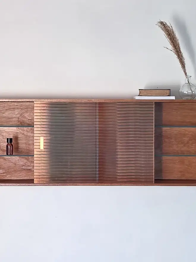 Shows a mid century Reeded glass wall cabinet with iridescent glass door to one side, revealing a natural wood vintage frame, with glass shelves on the interior