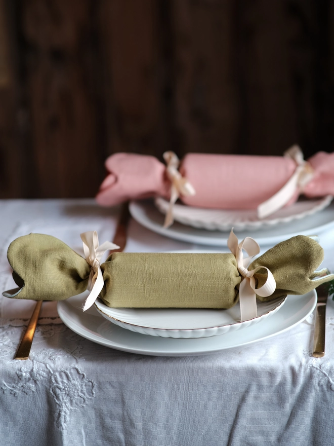 Reversible reusable linen Christmas crackers in soft pink, sage green, cream and muted festive colours, tied with natural ribbon and arranged on a family Christmas table