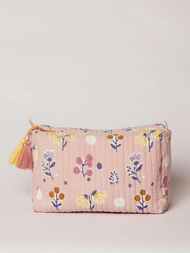 Dusty pink ditsy floral block printed quilted washbag with a yellow and a pink tassel hanging from the zipper puller
