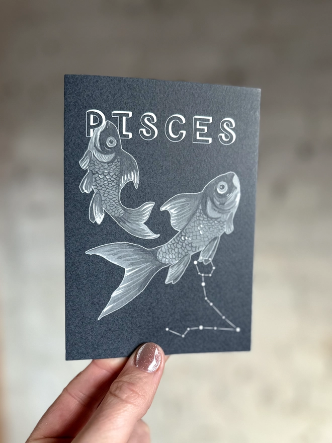 a greetings card featuring a greyscale illustration of a zodiac style couple of fish with the text “PISCES”
