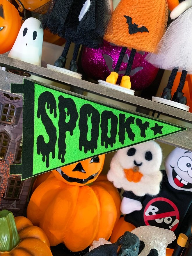 Image shows a felt pennant with the word ‘Spooky’ printed in black ink on bright green felt. The letters of the word are designed to look like the word is dripping. 