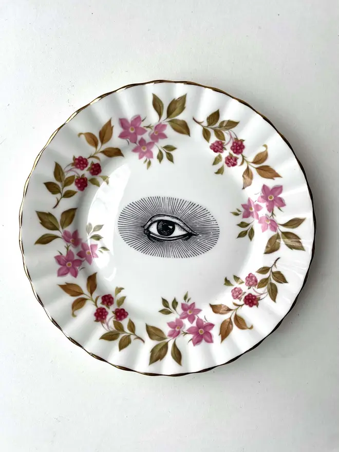 an ornate vintage plate with detailed patterned border, in the centre is printed an eye