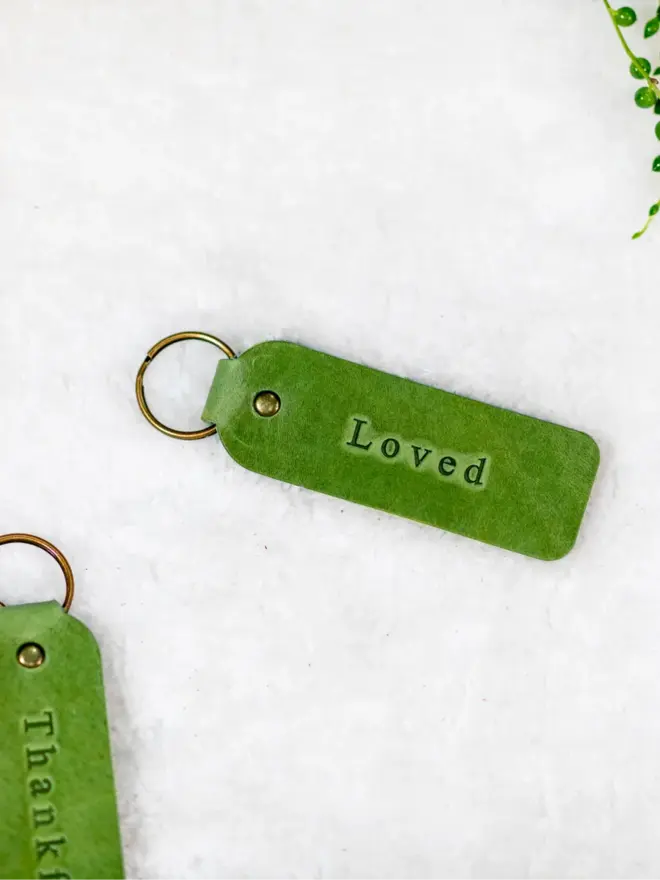 custom leather embossed keyring. light green leather keyrings embossed with 'loved' photographed against a white background.